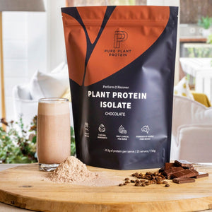 Pure Plant Protein plant protein isolate package with a glass of chocolate protein shake and ingredients on a wooden board.